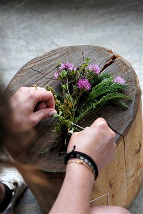 Eine Person bindet Blumen und Kräuter auf einem Holzblock. Die Blumen sind bunt und frisch.