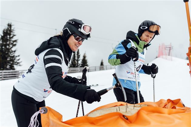 Zwei Skifahrer bereiten sich auf einen Wettkampf vor. Sie tragen Schutzkleidung und stehen auf einer verschneiten Piste.