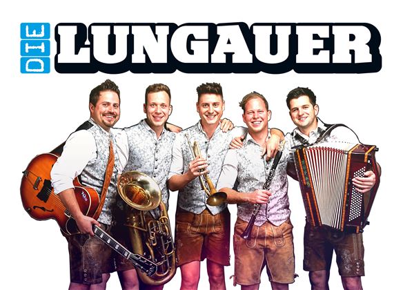 Fünf Musiker in traditioneller Tracht stehen zusammen und lächeln. Sie halten verschiedene Instrumente wie Trompete, Akkordeon und Gitarre in der Hand.