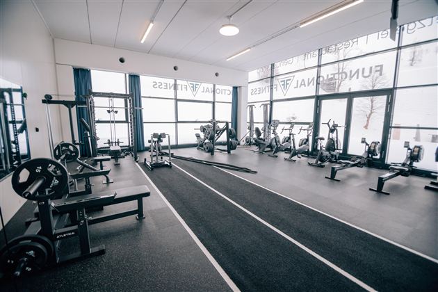 Ein modernes Fitnessstudio mit einer Vielzahl von Trainingsgeräten. Große Fenster sorgen für viel Tageslicht und eine motivierende Atmosphäre.