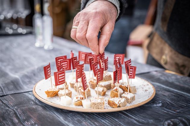 A plate with small snacks decorated with red flags. A hand reaches for one of the bites.
