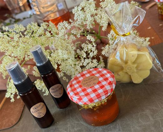 Two bottles with spray heads and a jar of honey are next to a bag with soaps and a white floral arrangement. The image shows handmade products in a cozy setting.