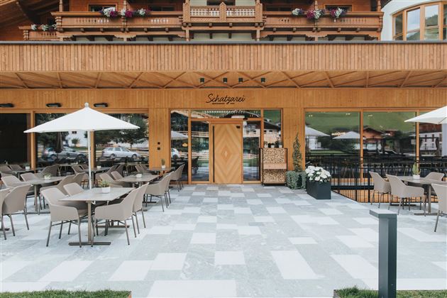 Ein modernes Restaurant mit Holzfassade und großen Fenstern. Draußen gibt es eine Terrasse mit Tischen, Stühlen und Sonnenschirmen.
