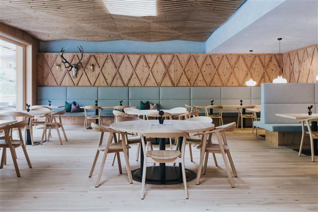 Ein modernes Restaurant mit Holzdekor und hellem Boden. Die Einrichtung umfasst runde Tische, helle Stühle und eine gemütliche Atmosphäre.