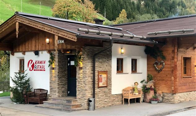 Ein gemütliches Holzgebäude mit Steinverkleidung und einem einladenden Eingangsbereich. Die Fassade ist mit Pflanzen und einer herzlichen Dekoration gestaltet.