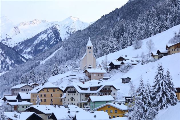 Eine malerische Winterlandschaft mit einem kleinen Dorf in den Bergen. Die Häuser sind mit Schnee bedeckt und umgeben von hohen, schneebedeckten Tannen.