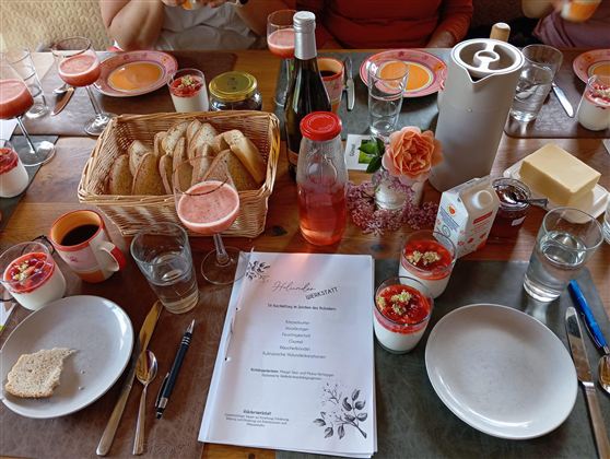 A set table with various foods and drinks. At the center are fresh rolls, desserts, and a menu card.