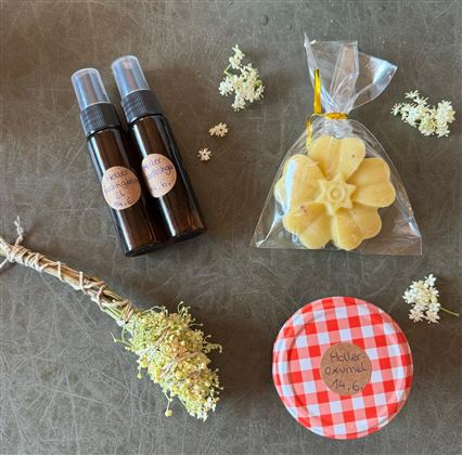 Two bottles with spray heads, a piece of soap in the shape of a flower, and a glass with a red checkered pattern. It includes some dried flowers and a small collection of blooms.