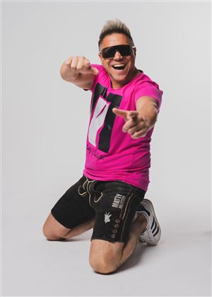 Ein männlicher Model sitzt kniend und trägt ein pinkes T-Shirt. Er trägt Sonnenbrillen und posiert enthusiastisch mit einem Lächeln.