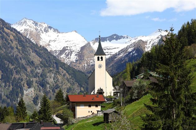 A picturesque mountain landscape with snow-covered peaks and a charming church in the foreground. Surrounded by green meadows and trees, the scene exudes tranquility and beauty.