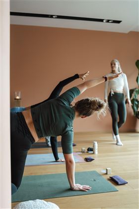 A group of women is doing yoga in a modern space. The floor is made of wood and the walls are in soft colors.