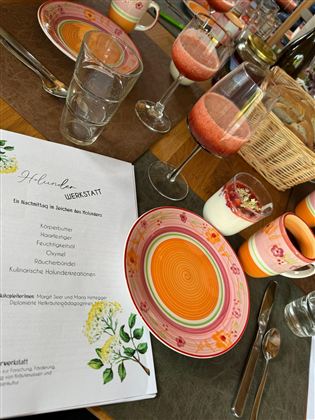 A festively set table with colorful dishes and various drinks. On the table lies a menu and several dessert glasses are visible.