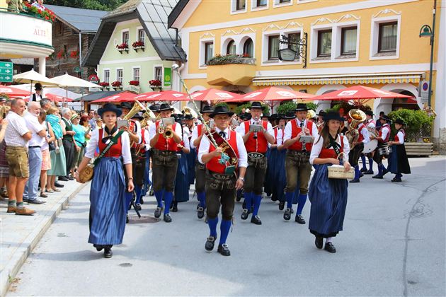 A traditional parade with people in traditional costumes. The group marches through a picturesque street while onlookers watch.