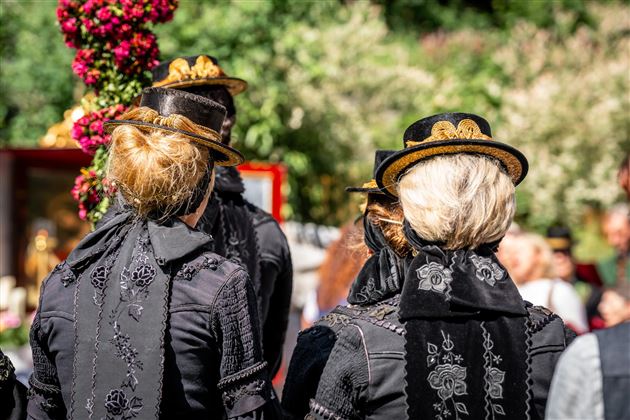 Eine Gruppe von Menschen in traditioneller schwarzer Kleidung steht im Freien. Ihre Hüte sind mit goldenen Verzierungen geschmückt.