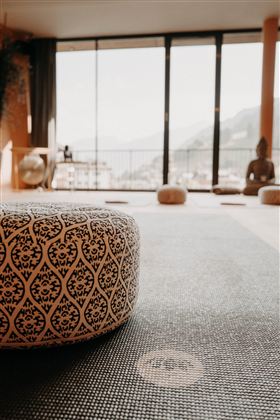 A cozy yoga room with a decorative cushion and a view of the mountains. Large windows let in plenty of light and create a relaxing atmosphere.
