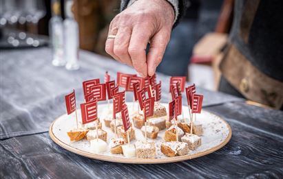 A plate with small snacks decorated with red flags. A hand reaches for one of the bites.