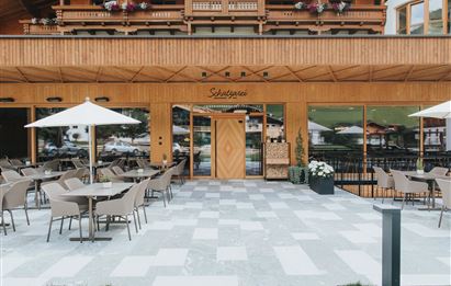 Ein modernes Restaurant mit Holzfassade und großen Fenstern. Draußen gibt es eine Terrasse mit Tischen, Stühlen und Sonnenschirmen.