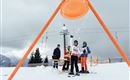 Ein Junge steht auf Skiern und jubelt, während Schnee herunterfällt. Im Hintergrund sind zwei weitere Personen und eine Skiliftanlage zu sehen.