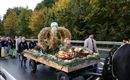 Eine festliche Parade mit einem Wagen, der mit Obst und Erntegaben geschmückt ist. Menschen in traditionellen Trachten begleiten den Wagen entlang der Straße.