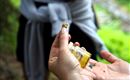 Eine Hand hält ein kleines Glas mit gelbem Inhalt. Im Hintergrund ist eine Person zu sehen, die aufmerksam zuhört.