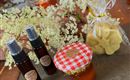 Two bottles with spray heads and a jar of honey are next to a bag with soaps and a white floral arrangement. The image shows handmade products in a cozy setting.
