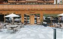 Ein modernes Restaurant mit Holzfassade und großen Fenstern. Draußen gibt es eine Terrasse mit Tischen, Stühlen und Sonnenschirmen.