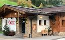 Ein gemütliches Holzgebäude mit Steinverkleidung und einem einladenden Eingangsbereich. Die Fassade ist mit Pflanzen und einer herzlichen Dekoration gestaltet.