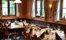 Ein gemütlicher Speisesaal mit holzgetäfelten Wänden und schön gedeckten Tischen. Die Umgebung ist warm und einladend, ideal für ein gutes Essen.
