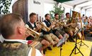 A brass band is playing cheerful melodies in a tent. The musicians are wearing traditional costumes and are surrounded by an audience.