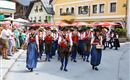 A traditional parade with people in traditional costumes. The group marches through a picturesque street while onlookers watch.