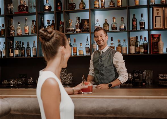 Ein freundlicher Barkeeper steht hinter der Bar und serviert einen Cocktail. Die Atmosphäre ist elegant und einladend.