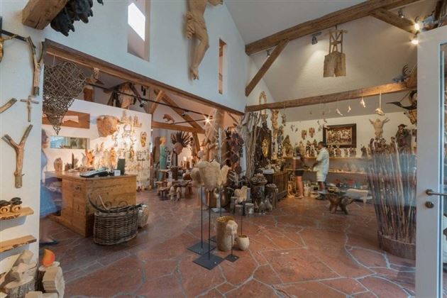 A craft store with many handcrafted wooden sculptures and decorative objects. The walls are adorned with various artworks, and in the background, a sales counter can be seen.