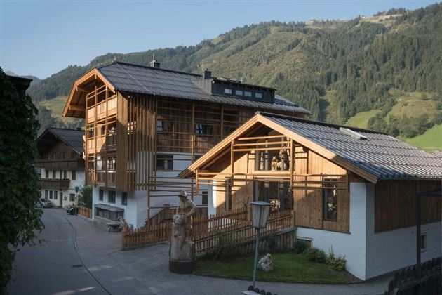 A modern alpine hut with a wooden facade in a picturesque mountain landscape. In the background, tall mountains and green fields are visible.