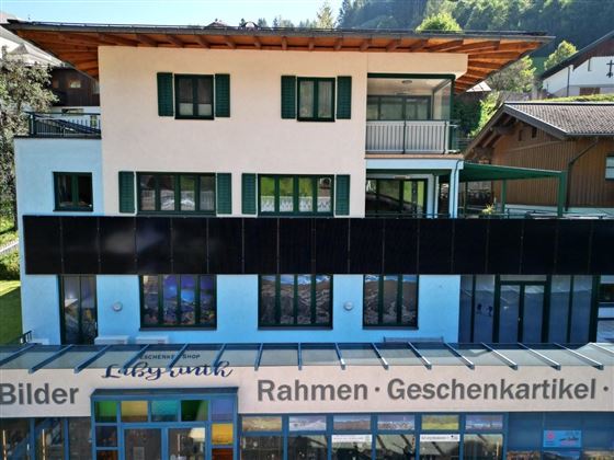 A multi-story building with green shutters. In the foreground, there is a shop for picture frames and gift items.