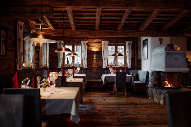 Ein gemütliches Restaurant mit Holzelementen und einer warmen Atmosphäre. Tische sind mit stilvollem Geschirr und Dekoration gedeckt, und im Hintergrund brennt ein Kamin.