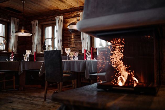 Ein gemütliches Restaurant mit holzverkleideten Wänden und einem offenen Kamin. Der Tisch ist festlich gedeckt mit Gläsern und roten Servietten.