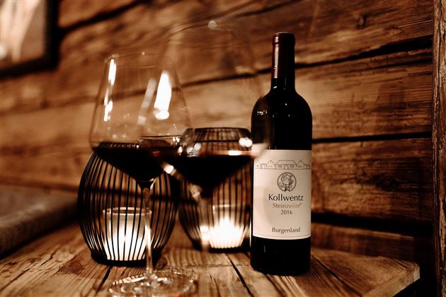 Ein eleganter Holztisch mit zwei Weingläsern und einer Flasche Rotwein. Sanftes Licht sorgt für eine gemütliche Atmosphäre.