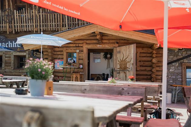 A rustic wooden building with an inviting entrance. Flowers and umbrellas are on the tables, creating a cozy atmosphere.