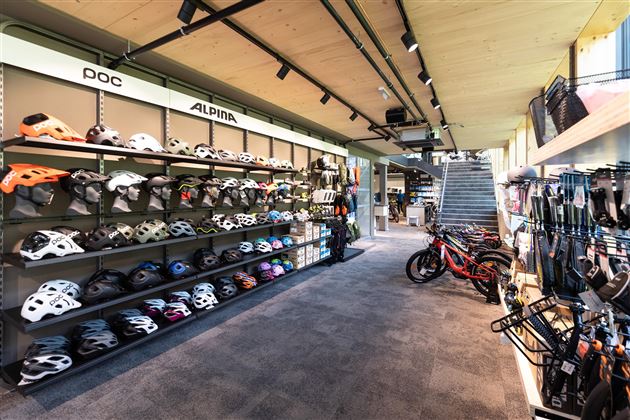 Ein modernes Sportgeschäft mit einer Auswahl an Fahrradhelmen und -zubehör. Im Hintergrund sind verschiedene E-Bikes aufgestellt.