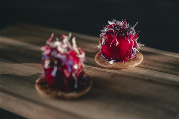 Two artistically decorated desserts on small plates. The sweet treats are adorned with colorful flowers and a glossy layer.