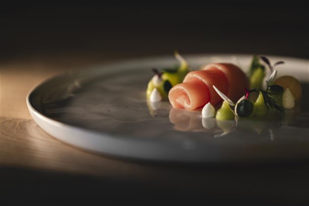 A stylish dish with salmon, artfully arranged on a white plate. Surrounded by colorful vegetables and various sauces.