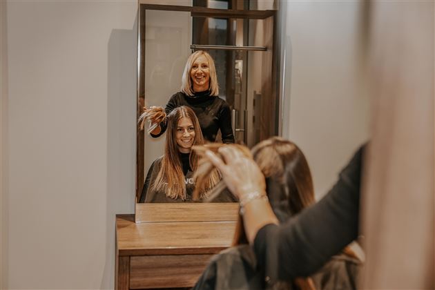 Eine Friseurin schneidet das Haar einer Kundin im Salon. Beide Frauen lächeln in den Spiegel.