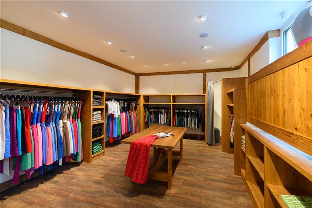 A well-organized clothing store with wooden shelves and colorful garments. In the center stands a large table, surrounded by clothing racks.