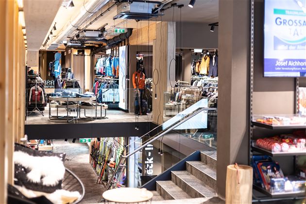 Ein moderner Bekleidungsladen mit einer großen Auswahl an Outdoor-Bekleidung. Die offene Raumgestaltung und die Treppe verleihen dem Geschäft ein einladendes Ambiente.