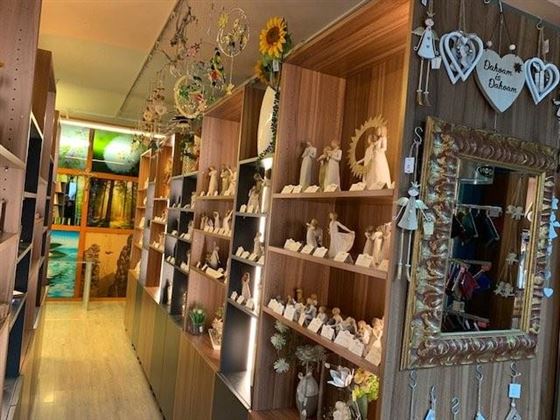 A cozy shop with shelves full of handcrafted figures and decorations. A large mirror hangs on the wall and the space has a friendly atmosphere.