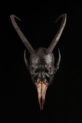 A mask-like face with long horns and a protruding tongue mouth. The depiction appears dark and eerie against a black background.