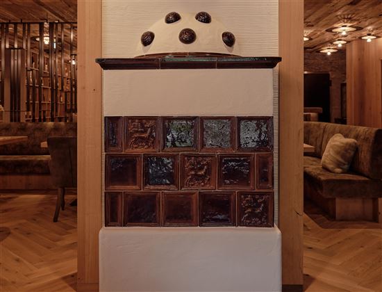 A stylish fireplace with ceramic tiles in various colors. The background features a modern interior design with wood and fabric elements.