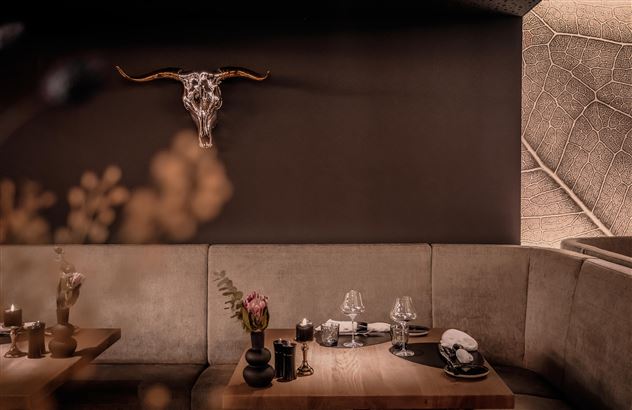 Ein stilvolles Restaurant mit einer gemütlichen Sitzgelegenheit. An der Wand hängt ein eindrucksvoller Tierkopf und die Tische sind elegant gedeckt.