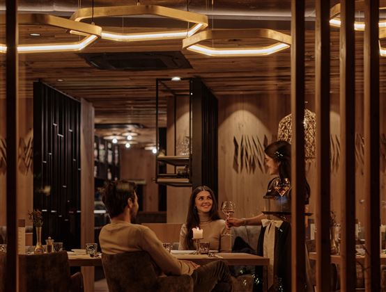 An elegant restaurant with warm lighting. Two guests enjoy their meal while a waitress serves at the table.