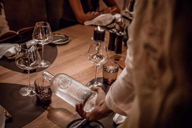 Ein eleganter Tisch mit Gläsern und einer Flasche Wasser. Die Atmosphäre wirkt gemütlich und einladend.